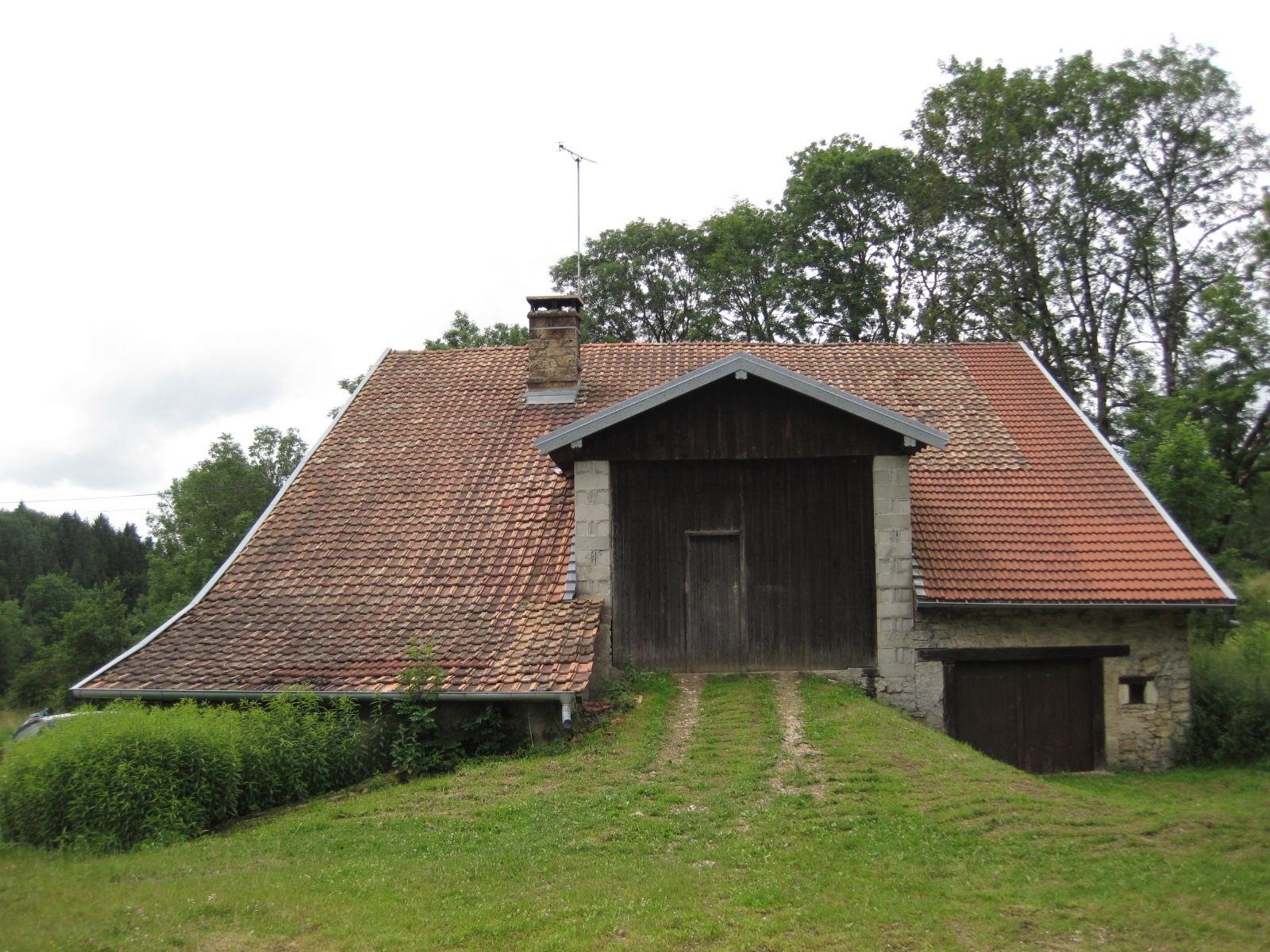 Ferme comtoise au long toit de tuiles, pignon bois et pierre